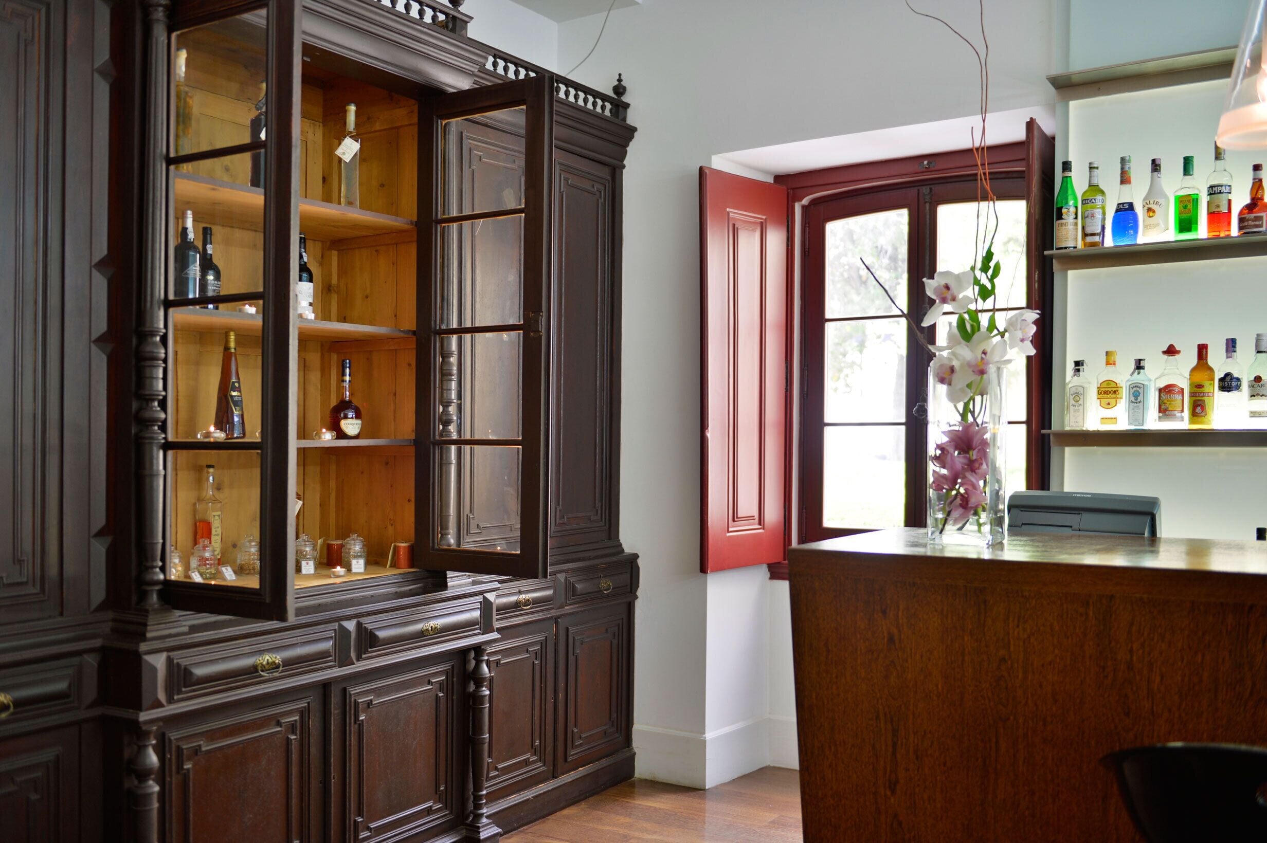 A wooden cabinet with glass doors, a red door, and a shelf with bottles.