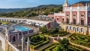 Un hotel con piscina, jardines cuidados y un edificio imponente con ventanas arqueadas y estatuas.