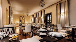 Un comedor amplio con varias mesas y sillas, candelabros elegantes y espejos grandes en las paredes.