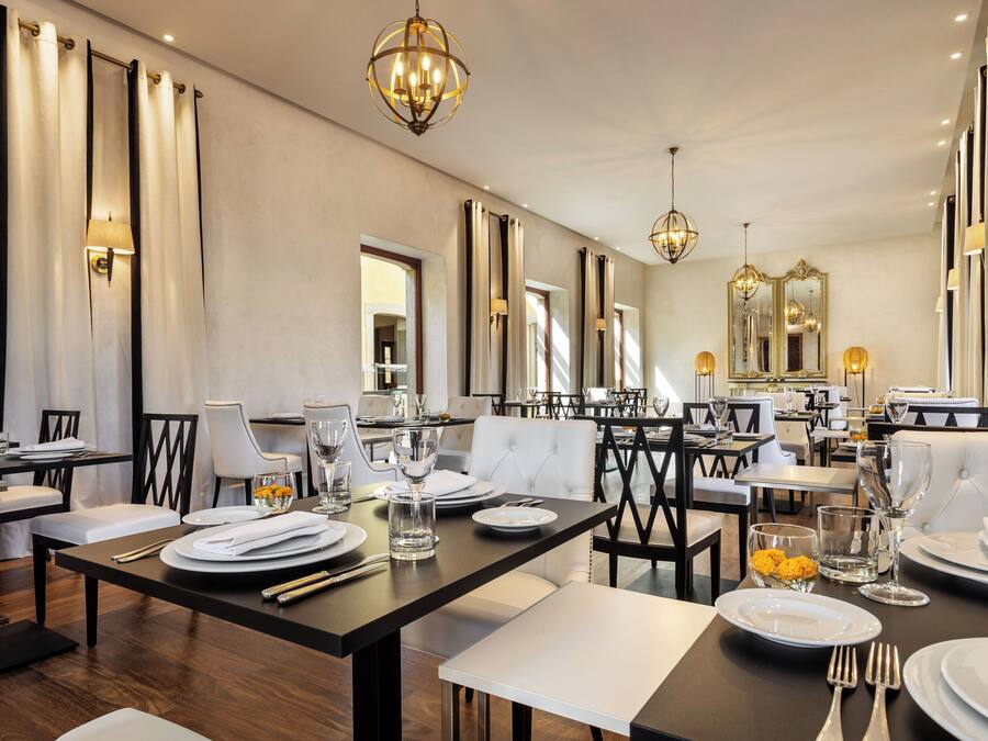 A spacious dining area with multiple tables and chairs, elegant chandeliers, and a large mirror reflecting the room.