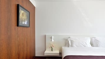 Una habitación de hotel con una pared de acento de madera, un cuadro enmarcado, una mesita de noche con un florero y una cama con ropa de cama blanca.