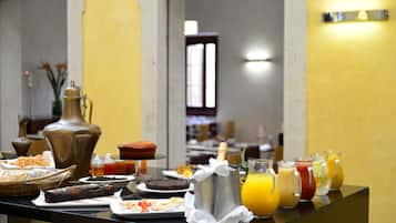 A buffet table with various breakfast items including pastries, a bottle of champagne, and multiple fruit juices.