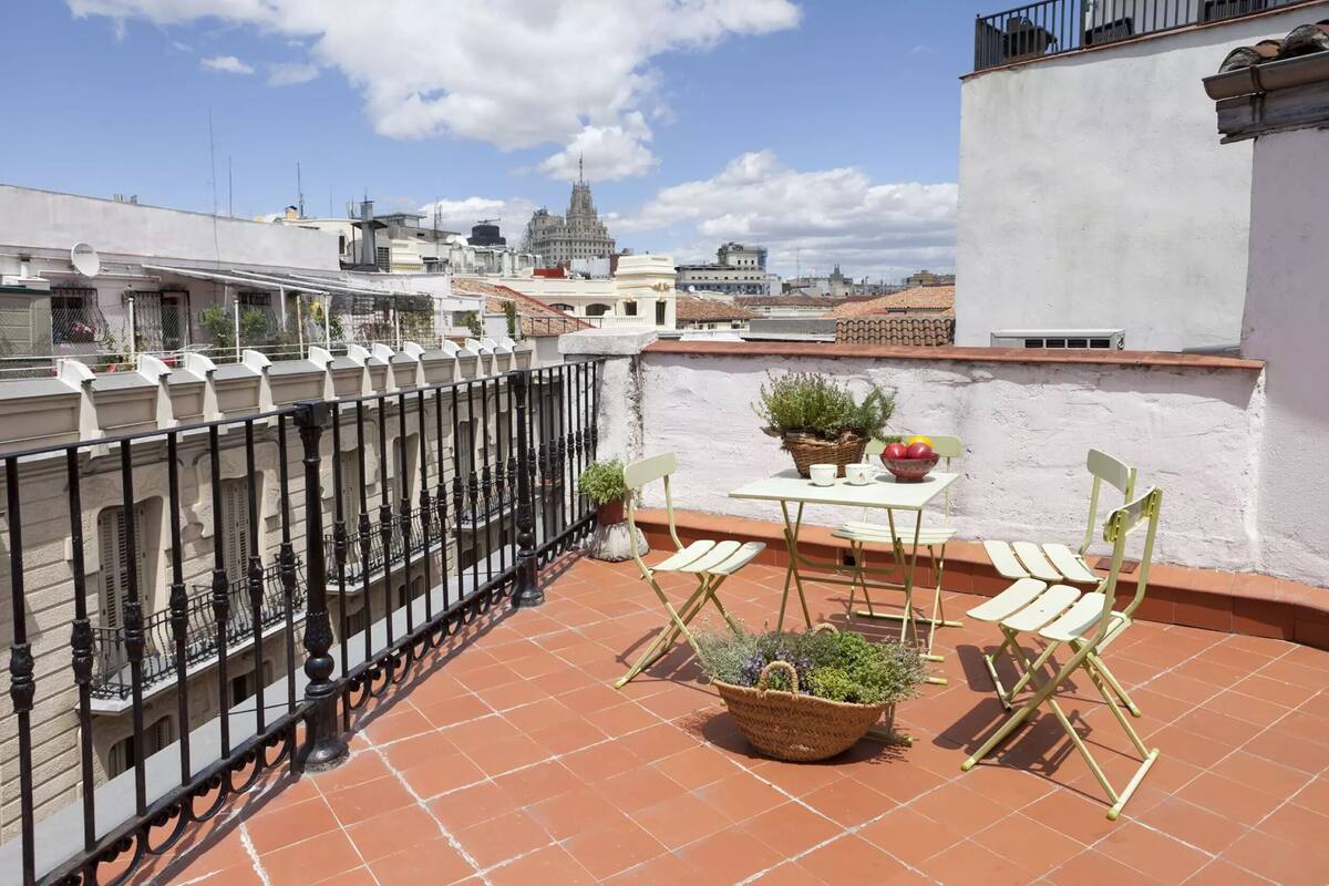 Una terraza con mesa y sillas, plantas en macetas y vistas de edificios urbanos.
