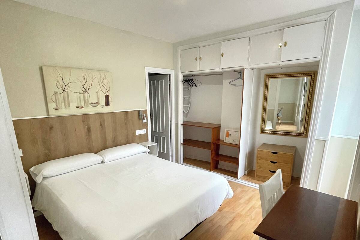 Un dormitorio con cama, escritorio, armario y espejo.
