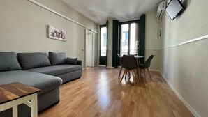A modern living room with a grey sofa, wooden flooring, a dining table with chairs, and a TV mounted on the wall. - Apartamentos Mayor Centro (Madrid)