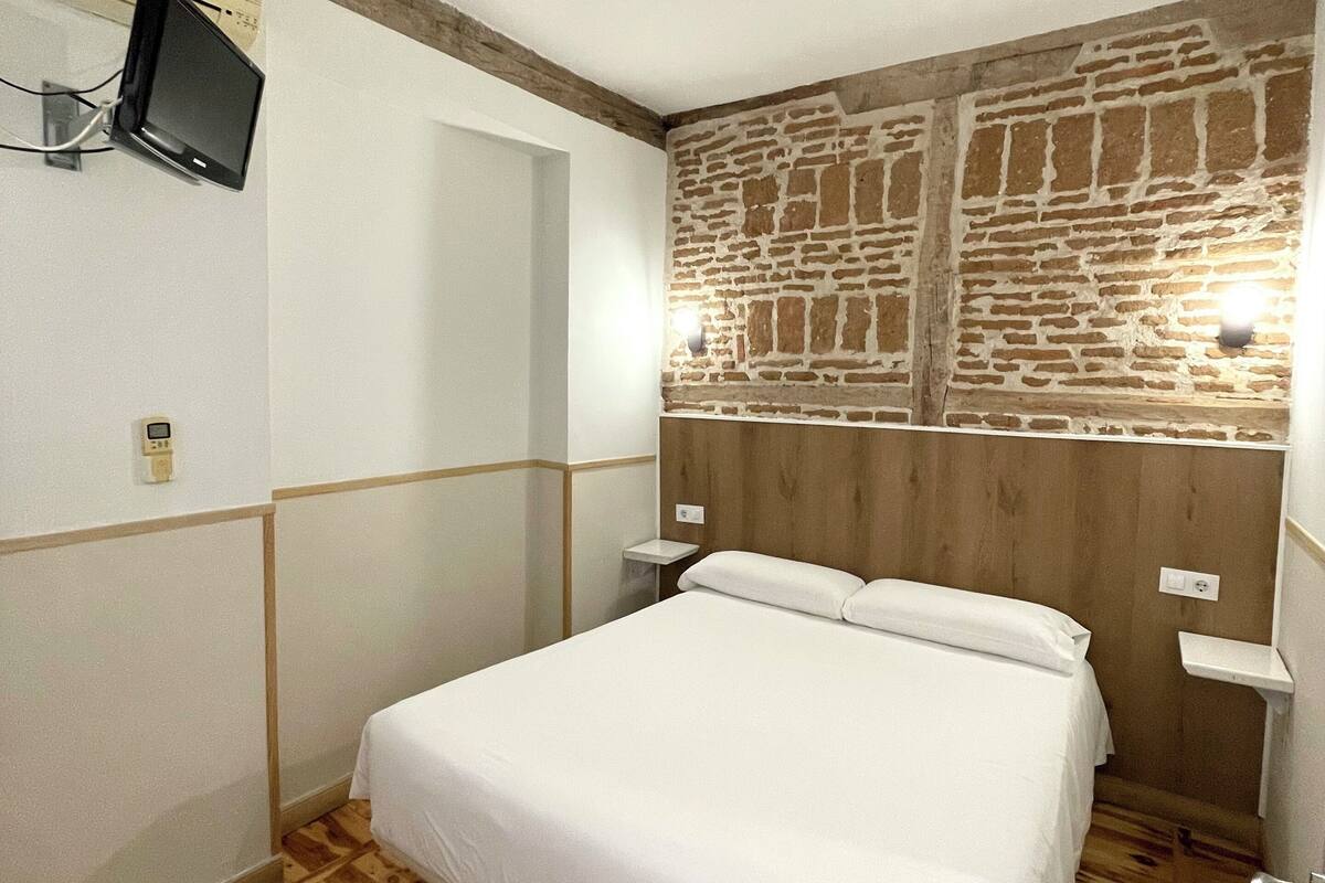 Habitación de hotel con cama, suelo de madera, pared de acento de piedra, televisor montado y mesita de noche.