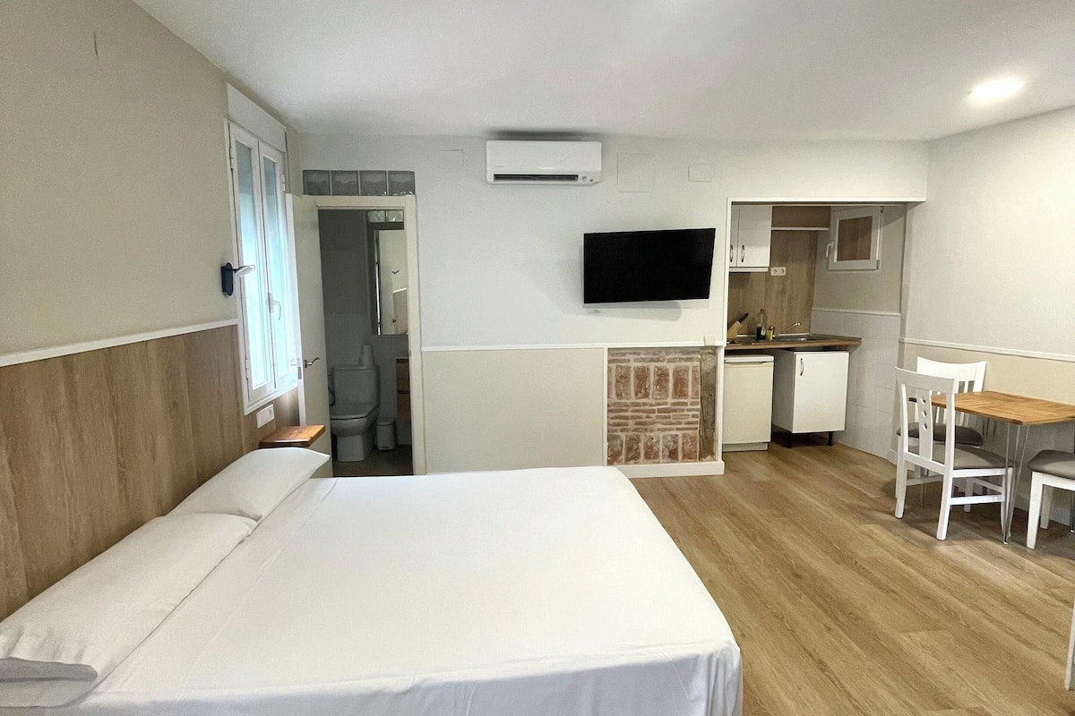 Habitación de hotel con una cama grande, un televisor montado en la pared, una pequeña kitchenette y piso de madera.