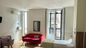 A hotel room with two beds, a red sofa, a dining area with a table and chairs, and a window with a view of the outside. - Apartamentos Mayor Centro (Madrid)