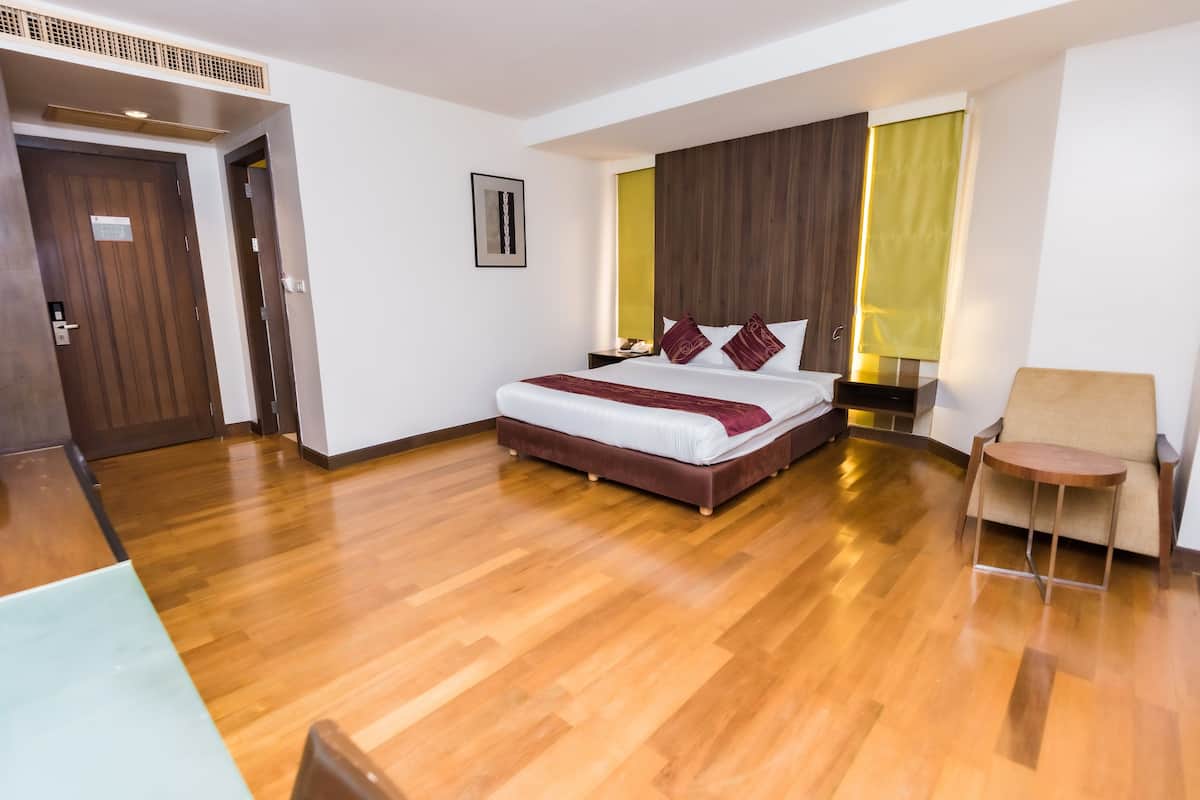 A modern hotel room with a wooden floor, a large bed with a white and brown bedspread, a wooden headboard, a bedside table, and a chair.