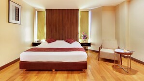 A hotel room with a large bed, a chair, a small table, and a nightstand. - Bally Suite Silom (Bangkok)