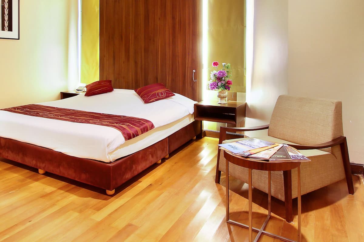 A hotel room with a large bed, a wooden floor, a small table with a chair, and a window with a view.