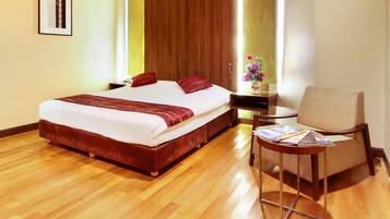 A hotel room with a large bed, a wooden floor, a small table with a chair, and a window with a view.