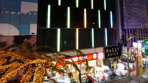 A modern hotel building with illuminated vertical lines on the facade, a visible restaurant named 'BALLY'S SILO' on the ground floor, and a 'BALLY'S SUITE' sign indicating a suite area. - Bally Suite Silom (Bangkok)