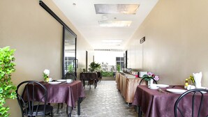 A dining area with tables set for two, featuring a patterned floor and a view of the outdoors. - Bally Suite Silom (Bangkok)