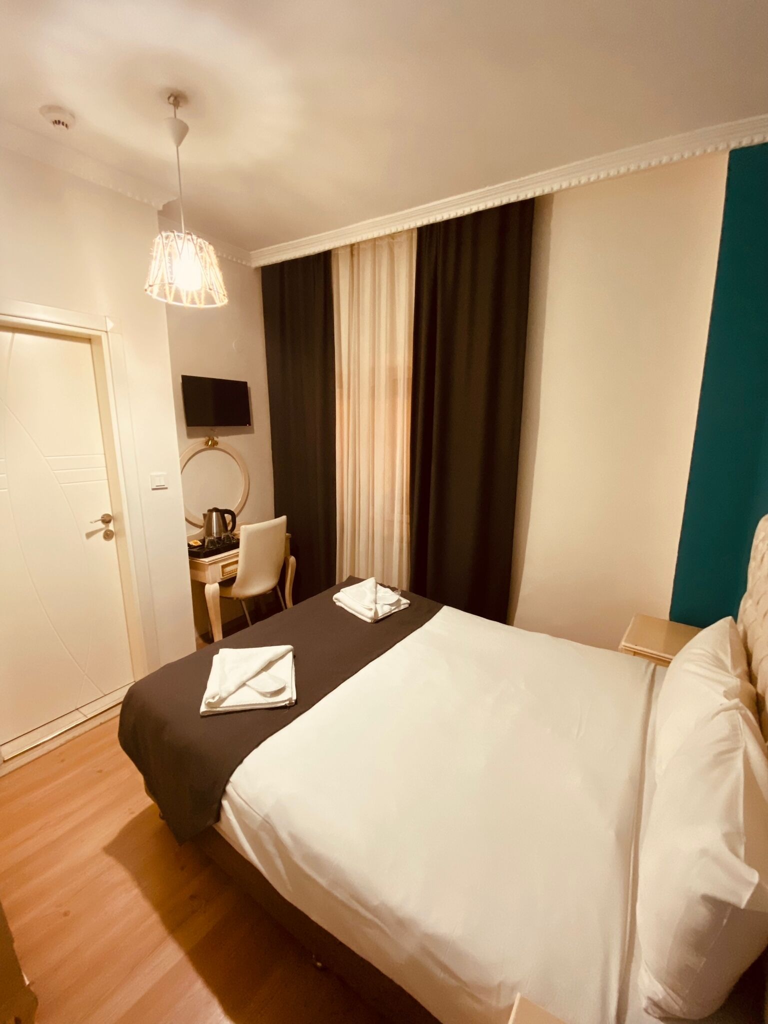 A hotel room with a bed, a desk with a chair, a television, and a window with curtains.