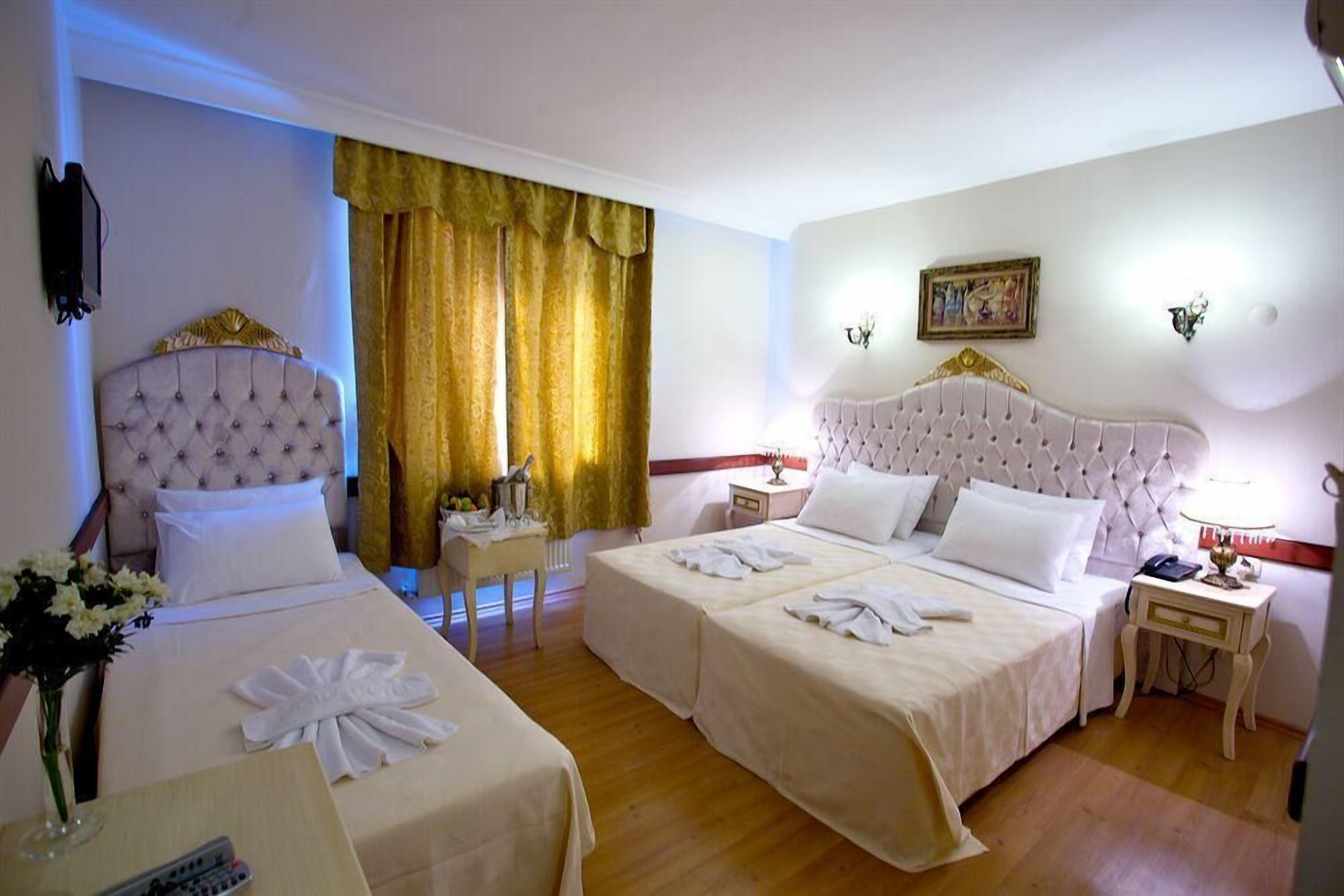 A hotel room with two beds, a bedside table with a lamp, a nightstand, and a painting on the wall.