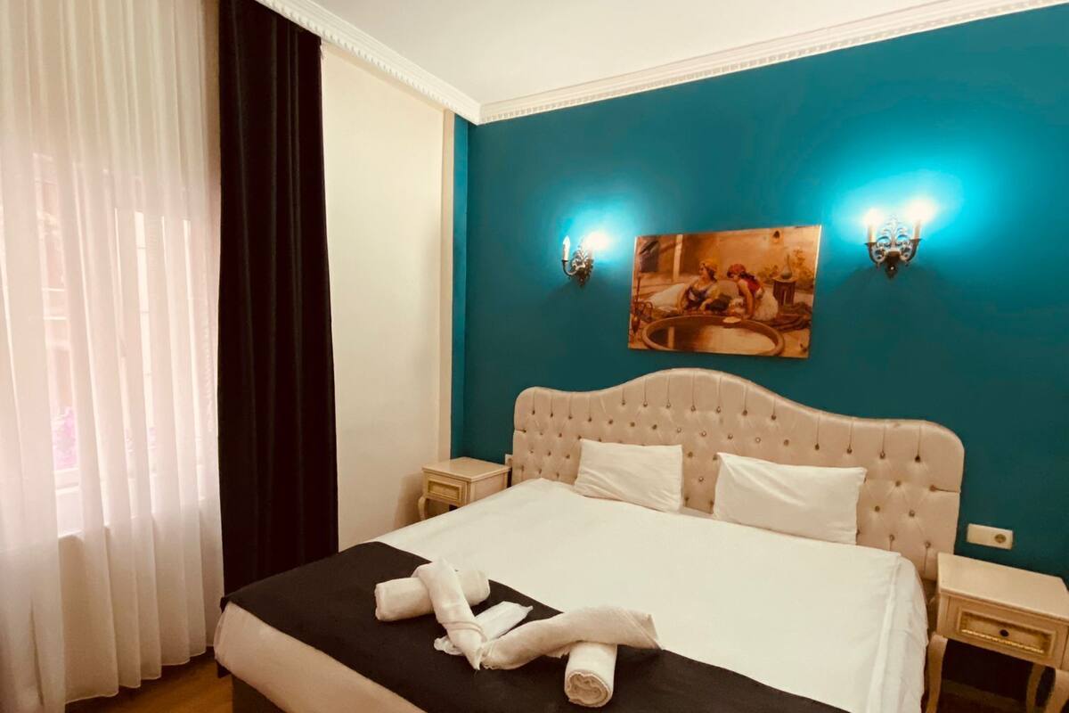 A hotel room with a bed, a nightstand, a wall-mounted lamp, and a painting.