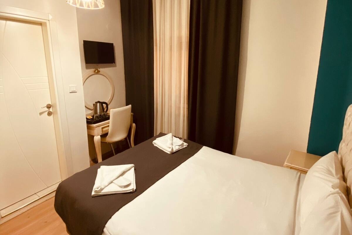 A hotel room with a bed, a desk with a chair, a television, and a window with curtains.