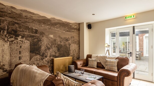 A room with a large mural of a castle, leather sofas, a coffee table, and a door with an exit sign. - The Pennington Hotel (Ravenglass)