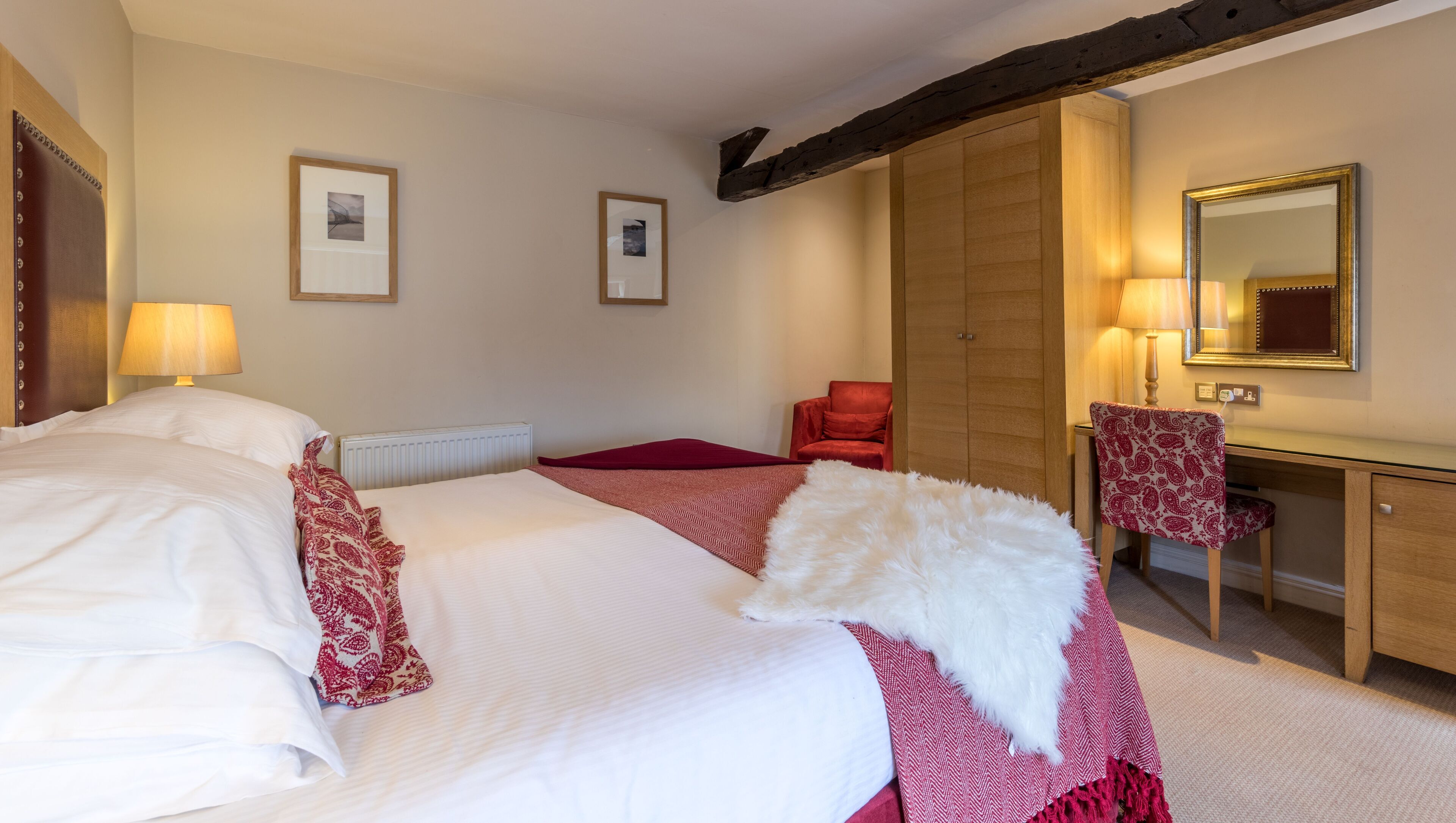 A hotel room with a large bed, a desk, a chair, and a mirror.