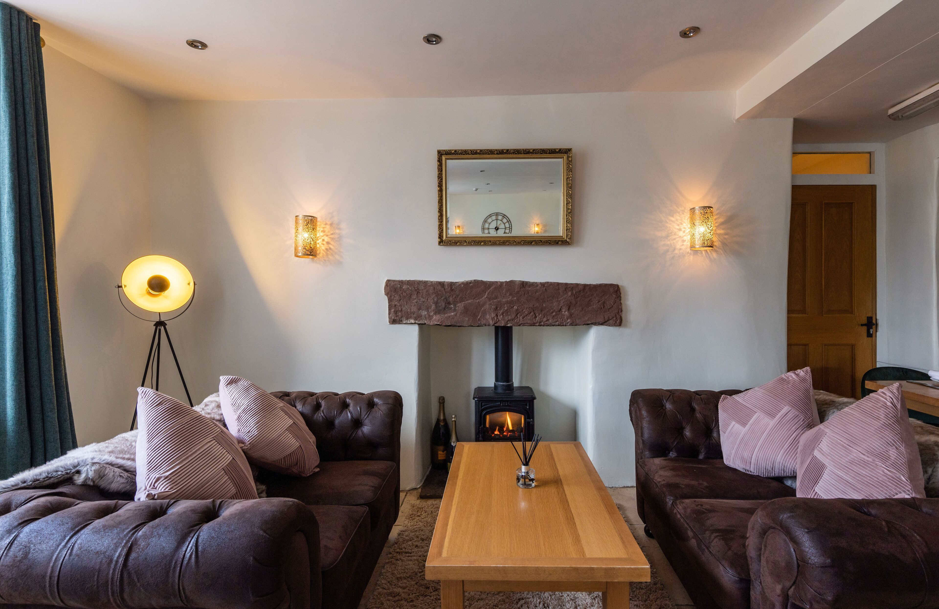 Ein gemütliches Wohnzimmer mit zwei Ledersofas, einem Holztisch, einem Kamin und Wandleuchten.