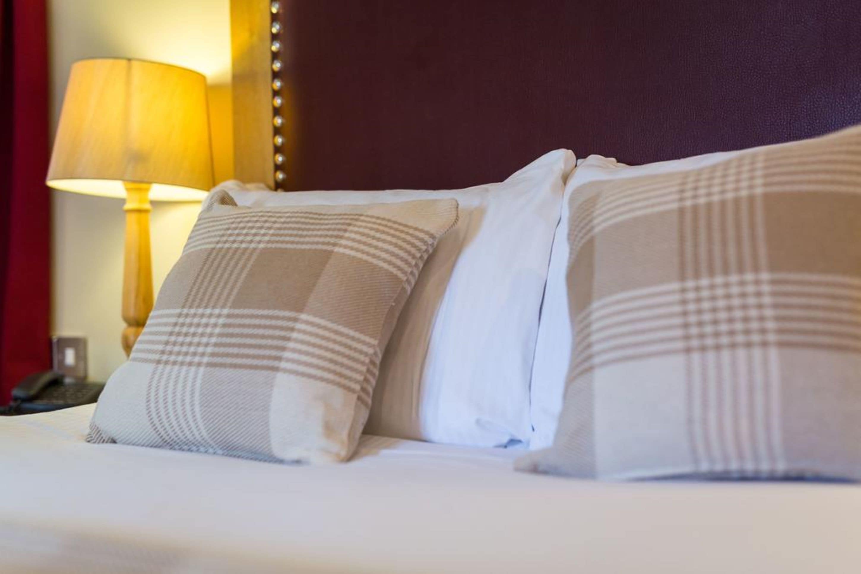 Una cama con dos almohadas, una lámpara y una pared con un detalle decorativo.