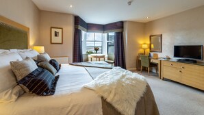 A hotel room with a large bed, a desk with a television, and a view of the beach through the windows. - The Pennington Hotel (Ravenglass)
