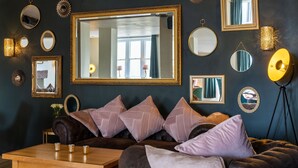 A dark-themed living room with a large mirror, multiple framed mirrors, and a leather sofa with cushions. - The Pennington Hotel (Ravenglass)
