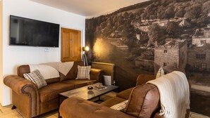A living room with a brown leather sofa, a coffee table, and a large mural of a town on the wall. - The Pennington Hotel (Ravenglass)