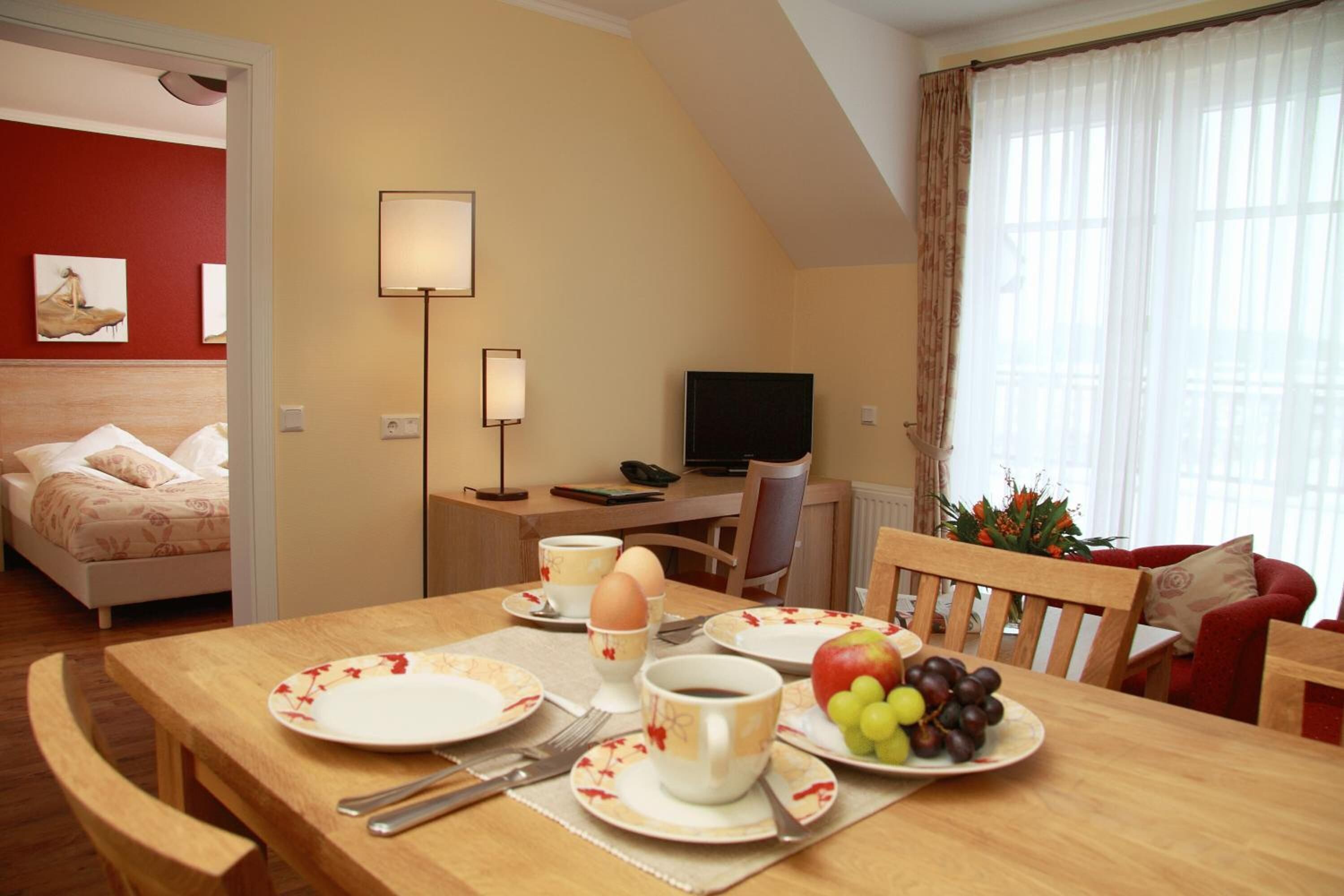 A hotel room with a dining area, a bed, a TV, and a window with curtains.
