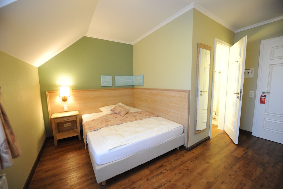 Ein Schlafzimmer mit einem Bett, einem Nachttisch und einem Beistelltisch. Es gibt zwei Türen, von denen eine geöffnet ist.