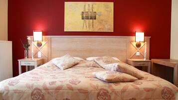 A hotel room with a bed, two bedside tables, a nightstand, a wall-mounted artwork, and a red wall.