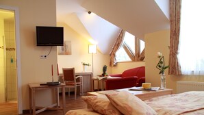 A hotel room with a bed, a desk, a chair, a TV, and a window with curtains.
