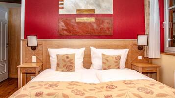 Cama doble con edredón floral, cabecera de madera, dos mesitas de noche con lámparas y una pared roja con arte abstracto.