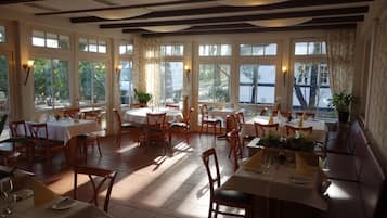 A restaurant with multiple tables and chairs, large windows, and a view of the outdoors.