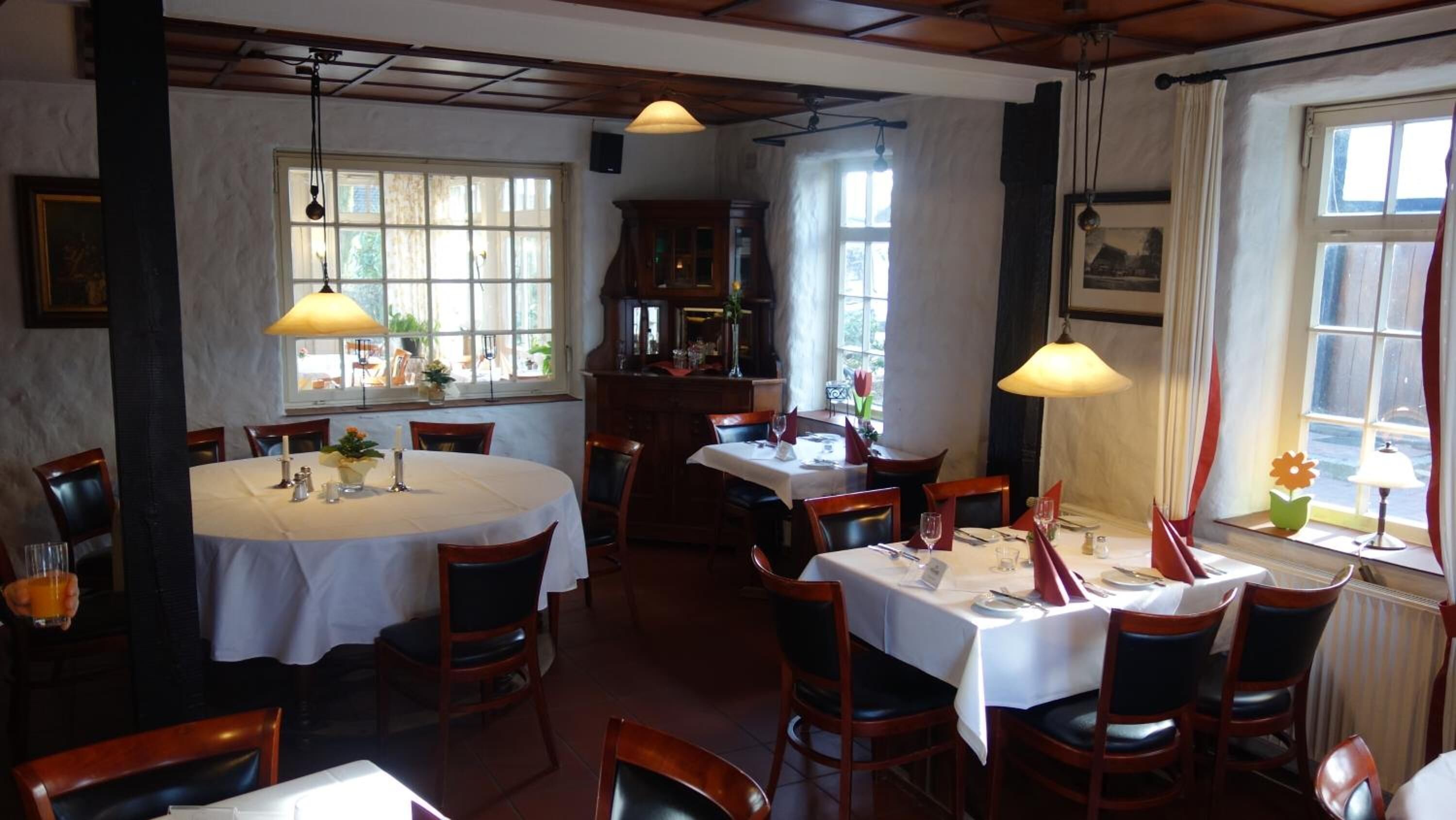 Een restaurant met ronde tafels, houten stoelen en hanglampen.