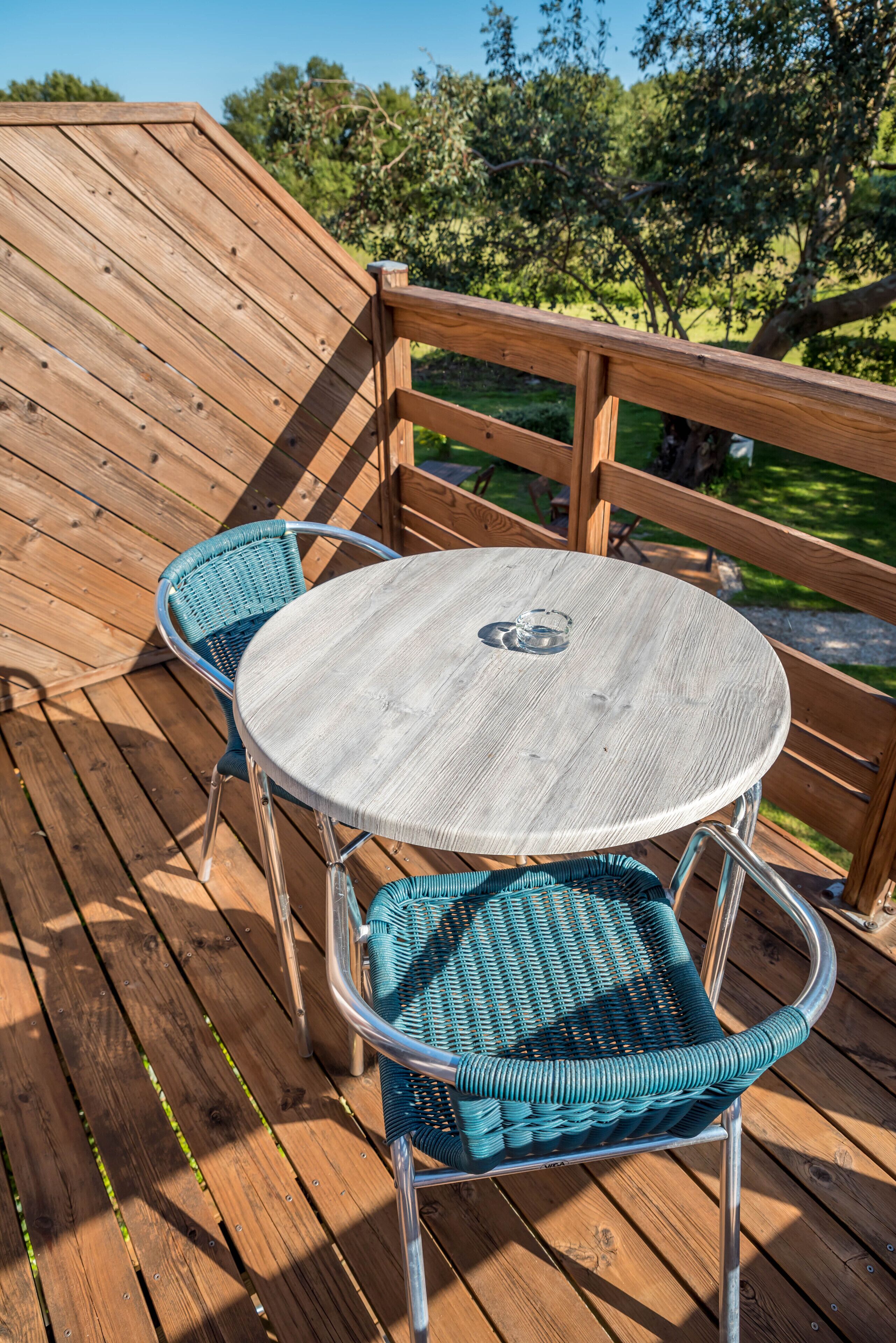 Eine Holzterrasse mit einem runden Tisch und zwei Korbstühlen.