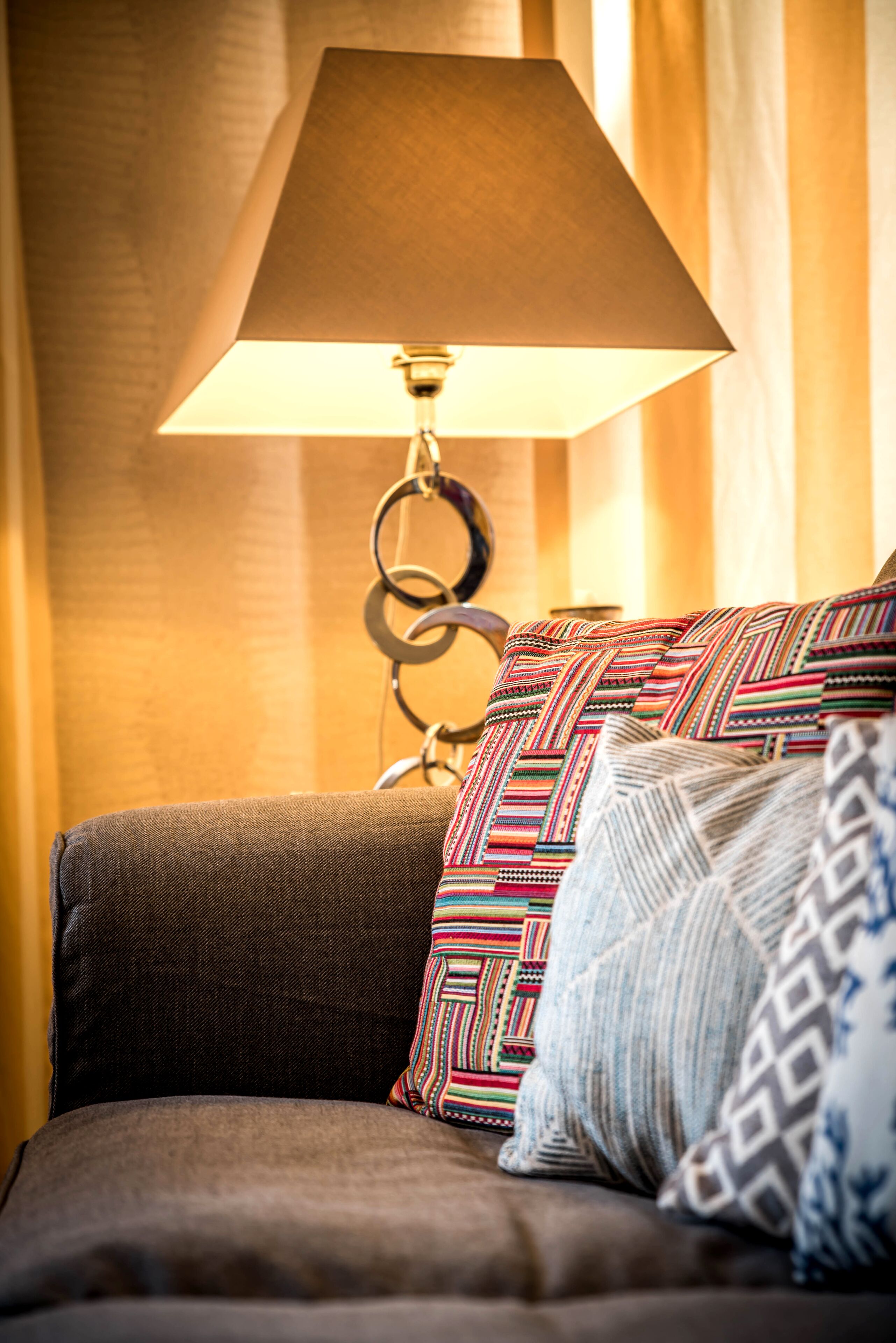 A bed with a dark brown headboard, a lamp with a conical shade, and patterned pillows.