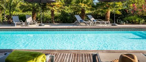 A poolside area with lounge chairs and umbrellas, surrounded by lush greenery.
