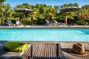 A poolside area with lounge chairs and umbrellas, surrounded by lush greenery. - Carnac Lodge Hotel & Spa (Plouharnel)
