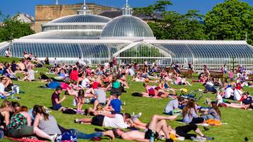 A large open-air structure with multiple domed sections, surrounded by a grassy area with people relaxing.