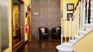 A hallway with a wooden floor, two black leather chairs, a white staircase, and patterned wallpaper. - Acorn Hotel (Glasgow)
