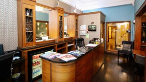 A reception area with a wooden counter, a refrigerator stocked with beverages, and a television mounted on the wall. - Acorn Hotel (Glasgow)