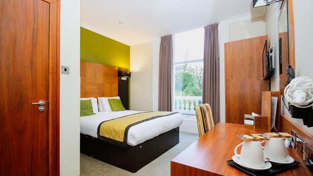 A hotel room with a bed, a wooden desk with two white teapots, a mirror, and a window with curtains. - Acorn Hotel (Glasgow)