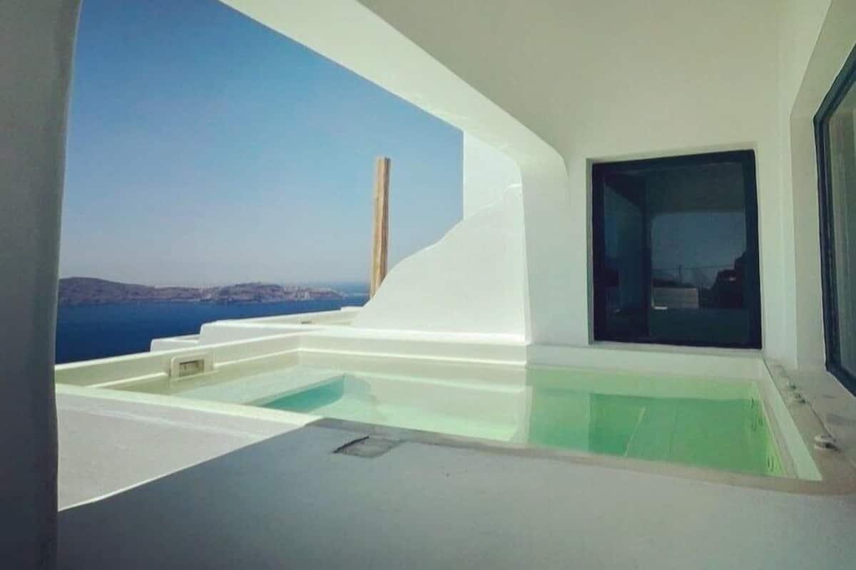 A modern, minimalist room with a large window offering a view of the sea and distant hills.