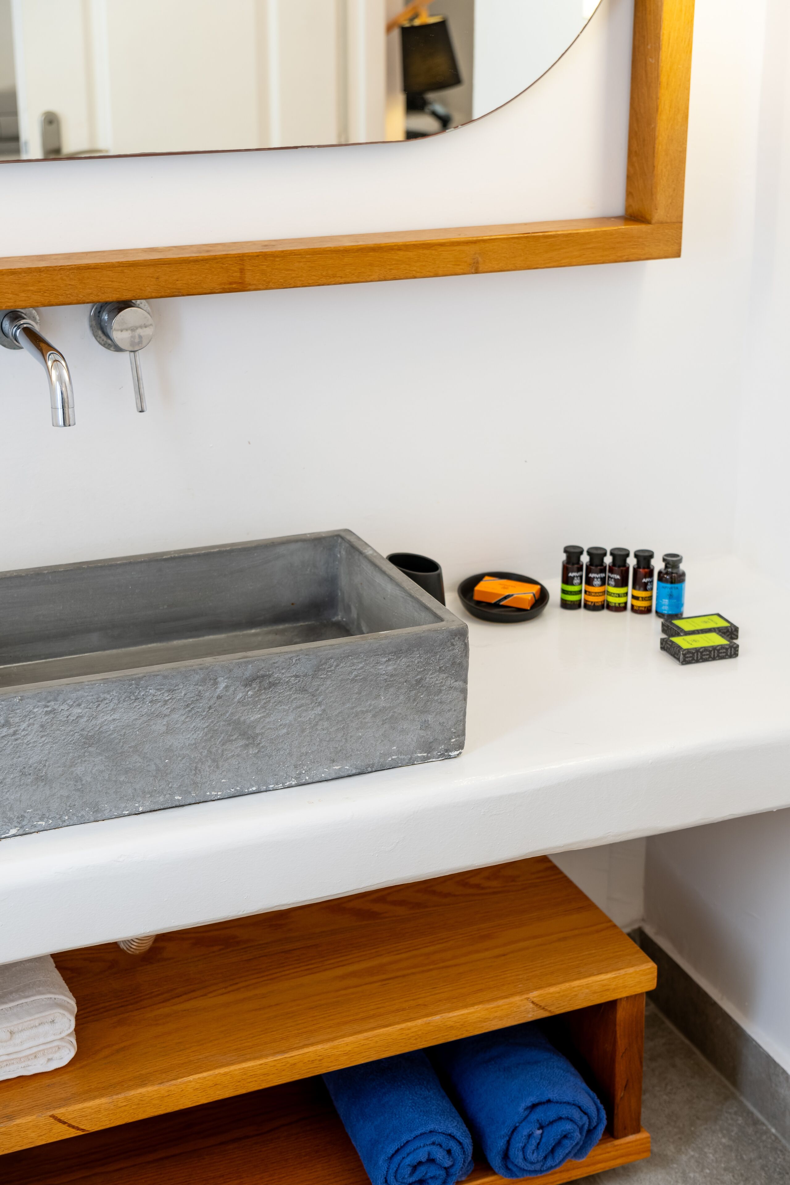 A bathroom with a rectangular sink, a wooden shelf with towels, and a mirror above the sink.