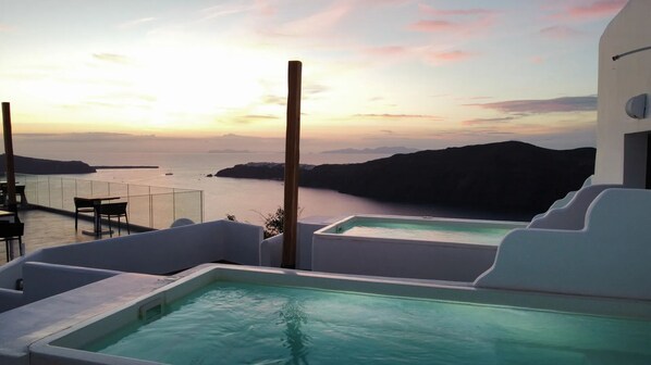 A rooftop pool with a view of the sea and a sunset.