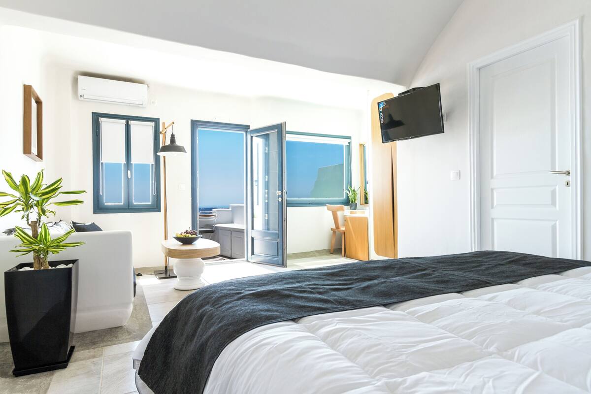 A modern hotel room with a large bed, a TV, a balcony with a view, and a potted plant.