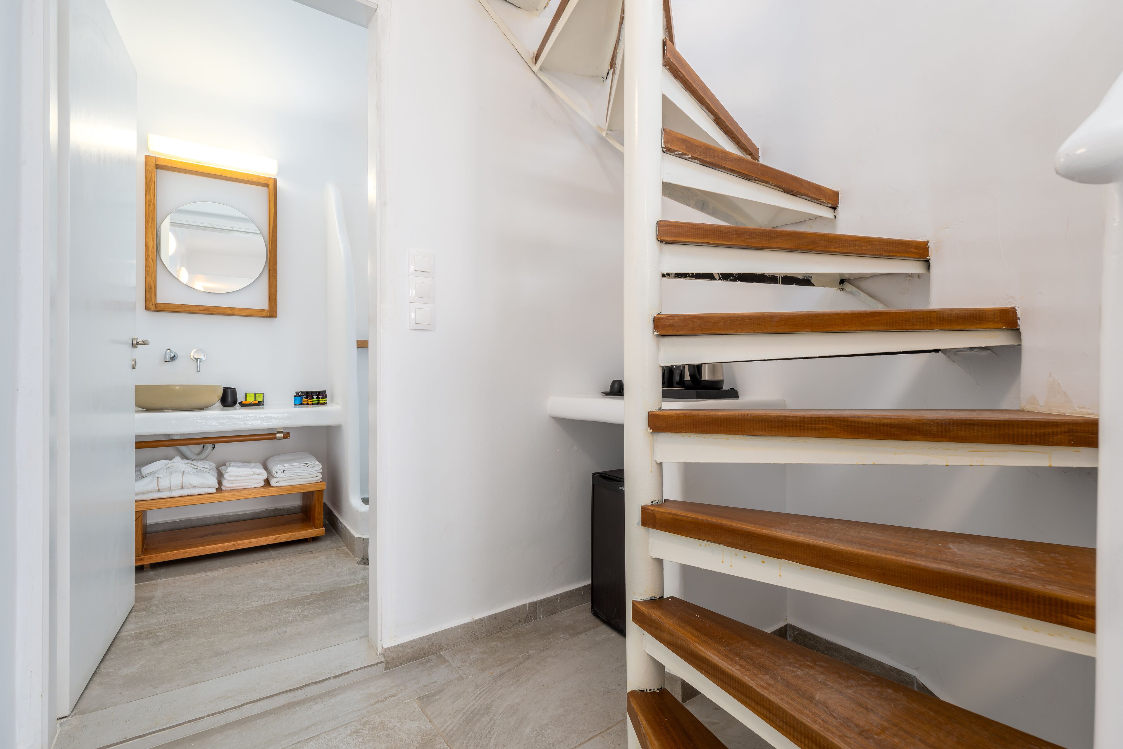 Ein modernes Badezimmer mit einer Holztreppe, einem Waschbecken mit Spiegel und ordentlich gefalteten Handtüchern.