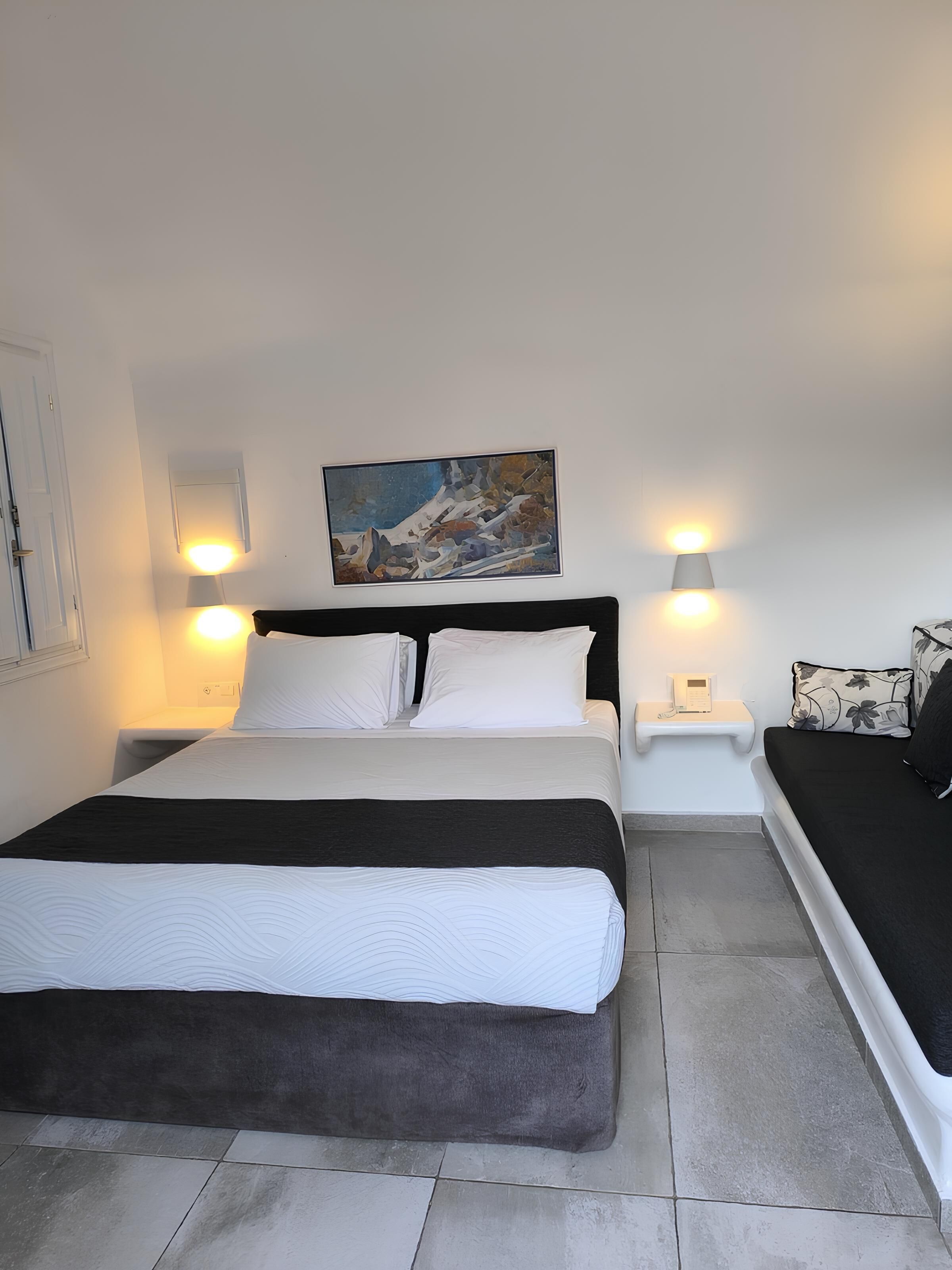 A neatly arranged hotel room with a large bed, bedside lamps, a painting on the wall, and a small bedside table.